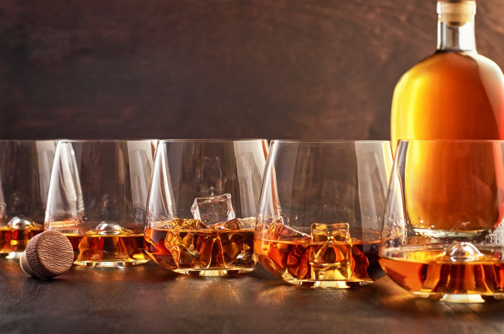 Zestaw szklanek do whisky i karafka na tle regału z alkoholami
