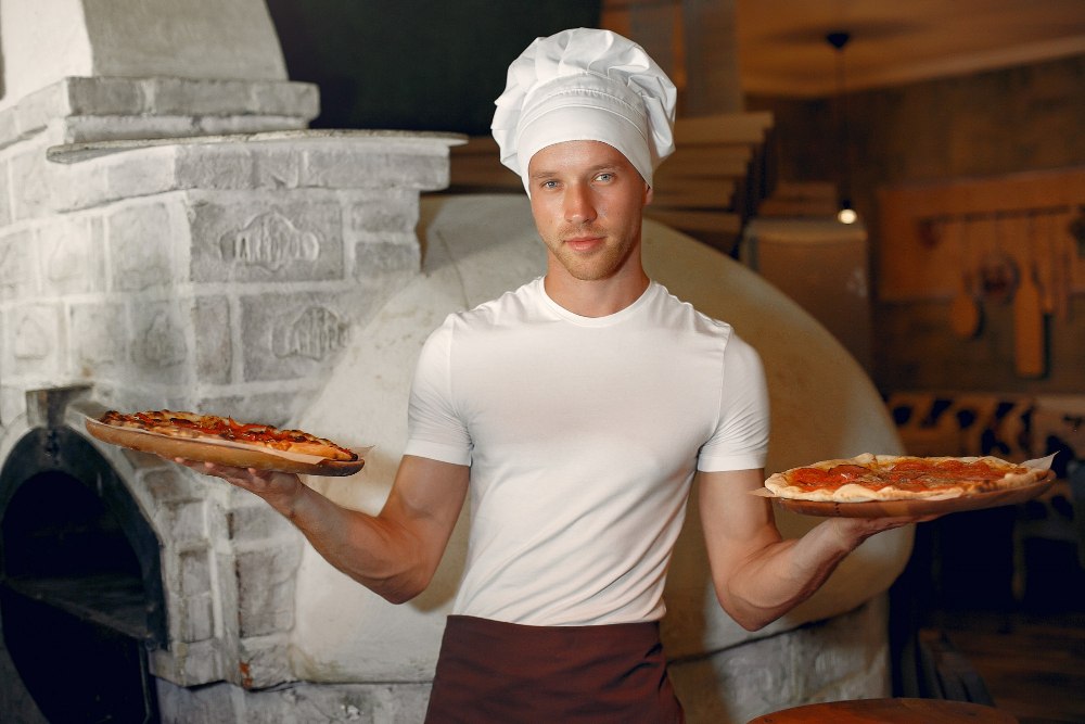 Pizzerman z przygotowanym ciastem i pizzą w profesjonalnej kuchni