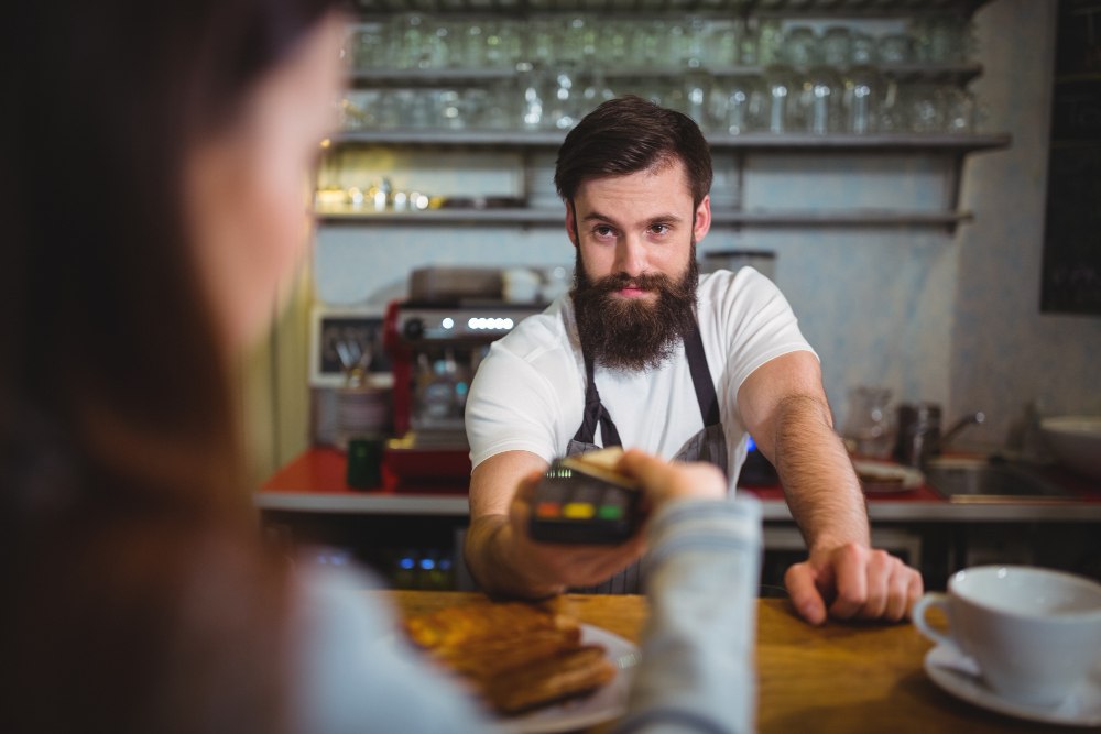 Gość w kawiarni odbierający espresso przygotowane z ekspresu ciśnieniowego