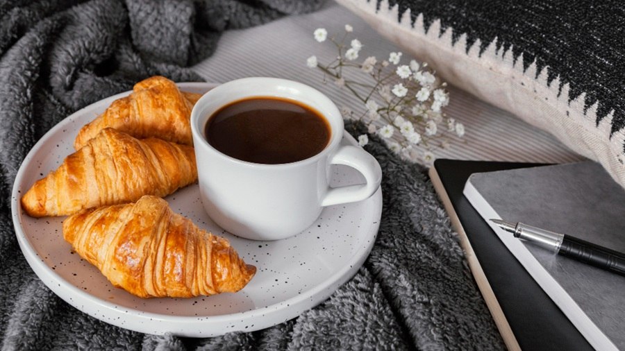 Śniadanie w kawiarni – filiżanka kawy i maślany croissant na białym talerzu, drewniany stolik, elegancka zastawa